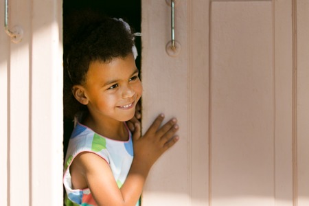 The black girl smiles in the doorway. Little African American girl looks at the street.の写真素材