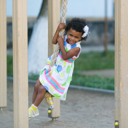 The girl is hanging on the sports rings. African American girl plays on a sports playground.の写真素材