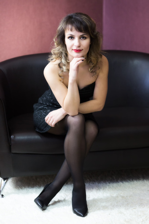 A girl in a short black dress sat on the sofa.の写真素材