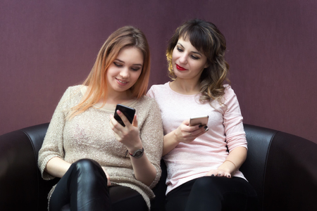 Close friends sit on the couch talking to each other and on the Internet.の写真素材