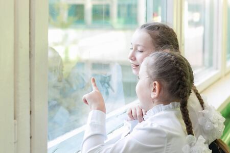 Girls schoolgirls look out the window into the street. Schoolgirls teenagers stand near window in the school hallway.の写真素材
