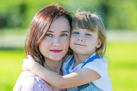 Portrait of a young mother with a baby. Young woman in summer park on a sunny day.
