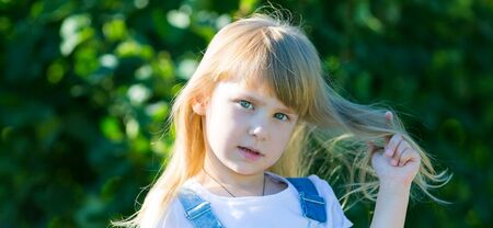 Little girl with long hair. Girl 4-5 years of age with green bushes.