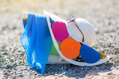 Women's hat bag and glasses on the beach. Beautiful bright female things for leisure hat bag sunglasses lie on a pebble beachの写真素材