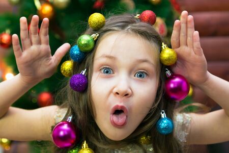 Little girl with a garland and Christmas balls in her hair her head laughing before Christmas Merry girl on new years eve.の写真素材