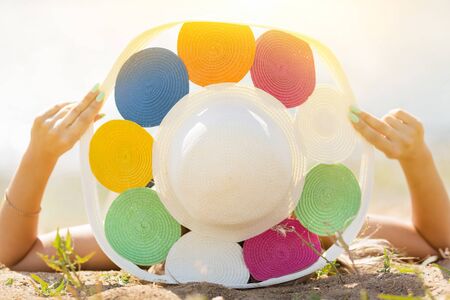 The girl in the hat lies on her back Woman in a big hat is sunbathing on the beach lying with her back on sand.の写真素材
