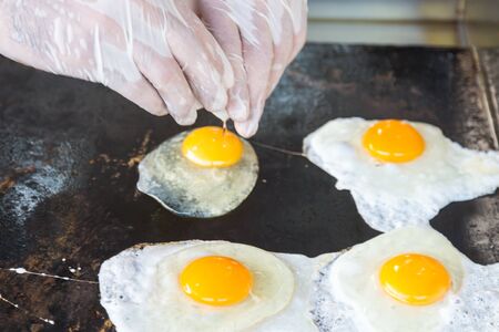 A man in white gloves fries eggs. The cook breaks egg and pours it into the panの写真素材