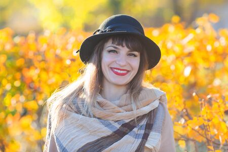 A pretty woman of 30-35 years old with a beautiful smile in a hat and coat near a yellow bush. Autumn portrait of a beautiful girl in a hat.の写真素材