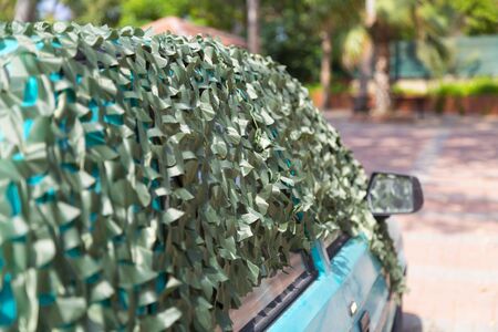 The car is covered with a protective camouflage net to protect from sunlight and high temperature. Car under camouflage net on the street.の写真素材