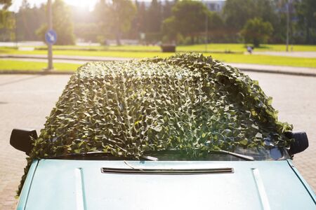 Car under camouflage net on the street. The car is covered with a protective camouflage net to protect from sunlight and high temperature.