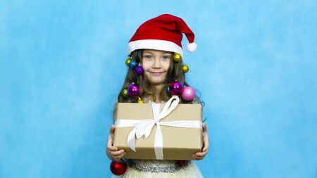 A child in a red hat with a New Year's gift in his hands. Girl in a Christmas hat with toys in her...