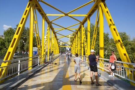 Passers-by go along the yellow bridge over the river.の写真素材