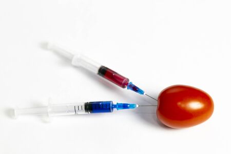 Two syringes with chemicals near a branch of tomatoes. Syringes with chemicals for fertilizing tomatoes on a white background.の写真素材