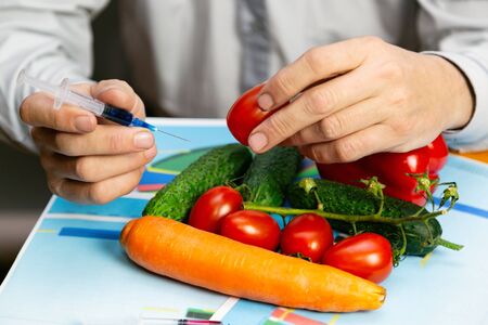 Chemical processing of vegetables, fertilizers and GMOs A man injects chemicals into tomato GMO fertilizers and chemicals with a syringe to increase the shelf life of vegetablesの写真素材