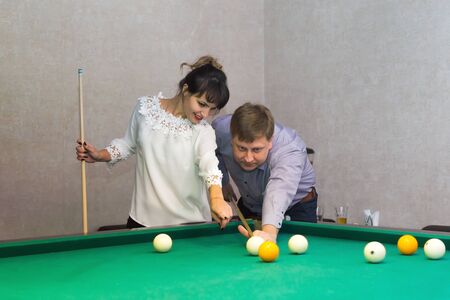 Adult man and a brunette woman stand near a table for a game of billiards.