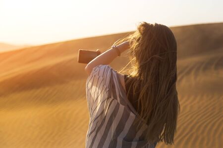 A young woman photographs a sunset in the desert on her smartphone.の写真素材