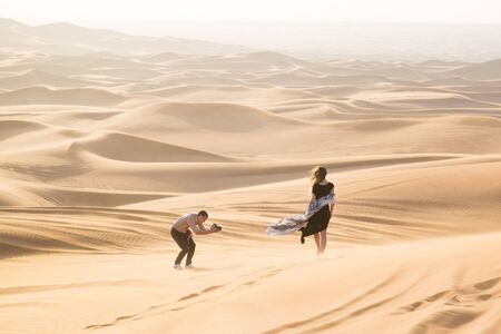 A man photographs a young woman in the sands of the desert an advertising shoot for a magazineの写真素材