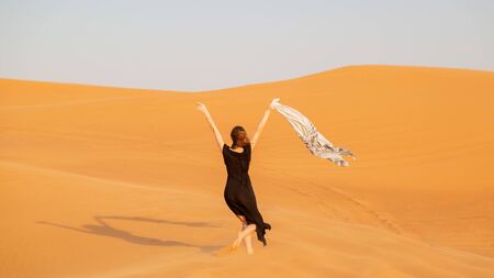 A woman in a black dress with a cloth in her hands in a strong wind alone in the desertの写真素材