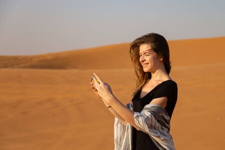 A girl in the desert takes a sunset on the phone young woman photographs a sunset in the desert on her smartphone.の写真素材