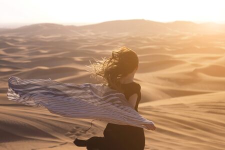 A girl with long hair in a black dress runs into the sunlight in the desert