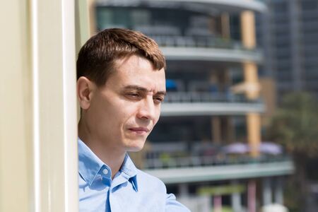 A man looks from the balcony at the city. A 35-40 year old Caucasian man stands on the balcony and looks at city life.の写真素材