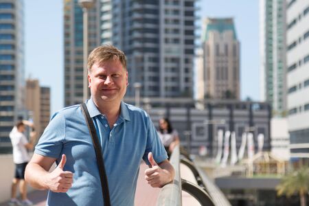A 35-40 year old caucasian man in a blue shirt smiles at the camera against the backdrop of a skyscraper, copy space.の写真素材