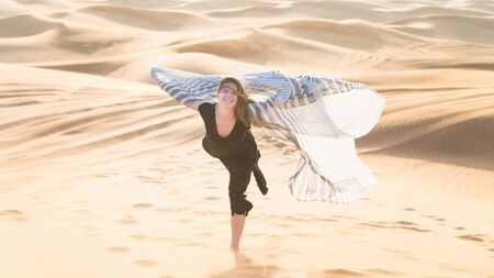 A girl in the desert stands on one leg. Dance of a girl in a black dress in the desert.の写真素材