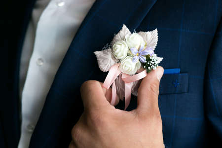 Male hand straightens the boutonniere on the grooms suit
