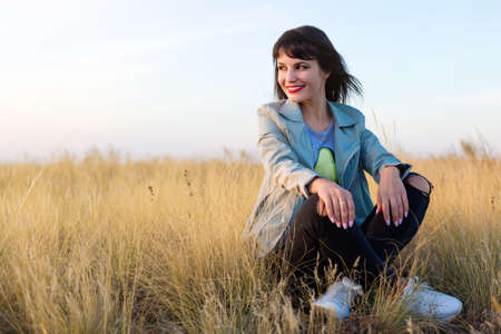 Brunette woman sitting in yellow steppe grass.
