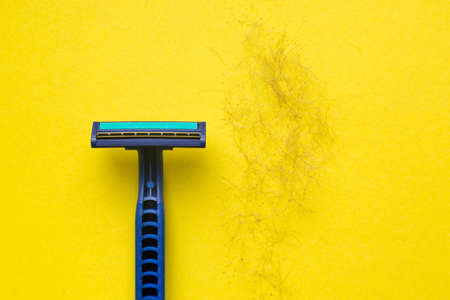 Men's razor and a bunch of hair and dirt on a yellow background.の写真素材