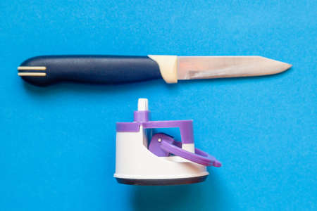 Kitchen knife and compact knife sharpener on blue background.