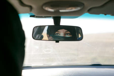 Brunette muslim woman in the reflection of the car mirror in the salon.の写真素材
