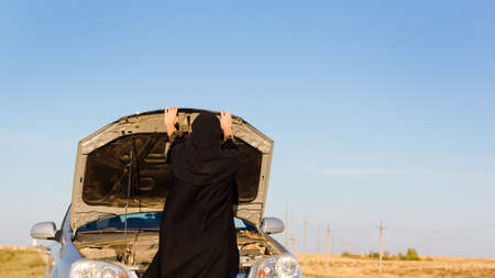 Muslim woman near open hood car on empty roadの写真素材