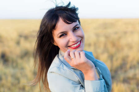 Brunette girl in a blue jacket in a field with yellow grass.の写真素材