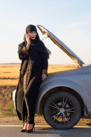 Portrait of a muslim woman calling on the phone near the car.