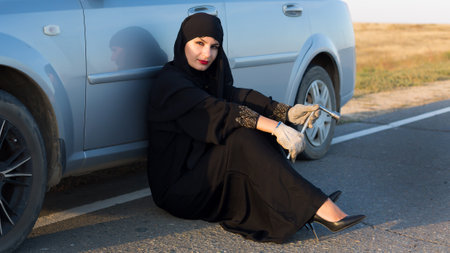 Woman driver sits on asphalt near a broken car.の写真素材