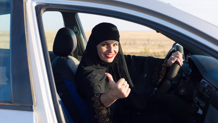 Woman driving car smiling and showing thumb gesture.