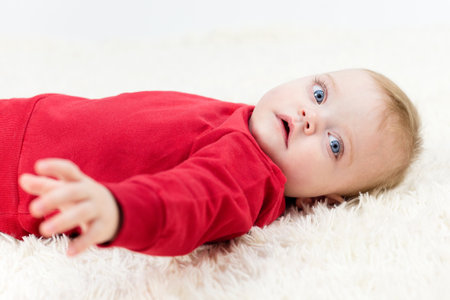 A small child lies on his back on the floor on a white blanket.の写真素材