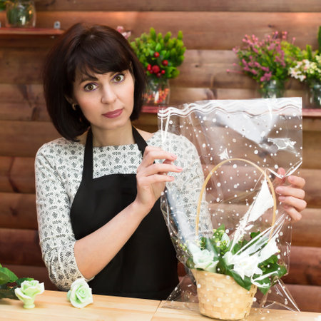 Florist lays a basket of flowers in transparent gift wrap.の写真素材