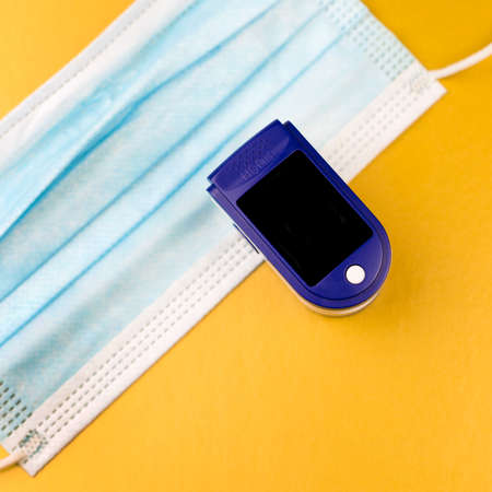 Oximeter and protective medical mask on gold background. Copy space.
