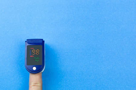 Oximeter on the finger of a mans hand on a blue background
