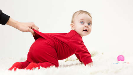 The parent holds the baby's clothes with his hand so that he does not crawl far. Motherhood parenting concept.の写真素材