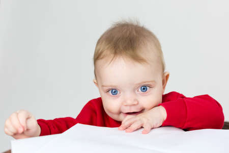 Child in red clothes plays with paper while standing at the tableの写真素材