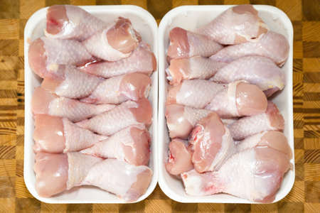 Chicken drumsticks frozen in a container on a wooden cutting board,の写真素材