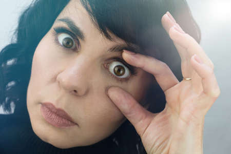 Woman opens her eyes with her fingers for inspection close-up.