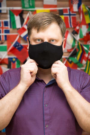 Adult blond man in medical mask against the background world flags.の写真素材