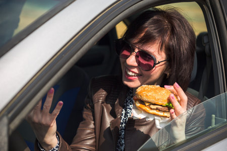 Woman with food in hand driving a car.の写真素材