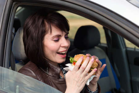Smiling woman in a car driving with a burger.
