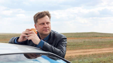 A man eats leaning on the roof of a car, against the blue sky. Copy spaceの写真素材