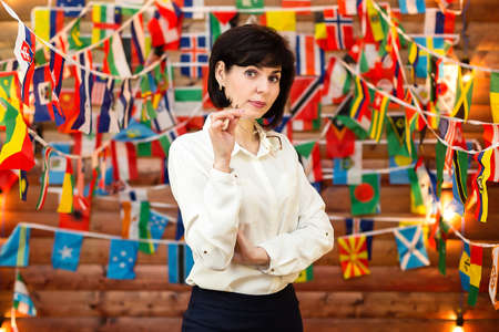 A strict woman in a white blouse holds glasses against the background of flags.の写真素材